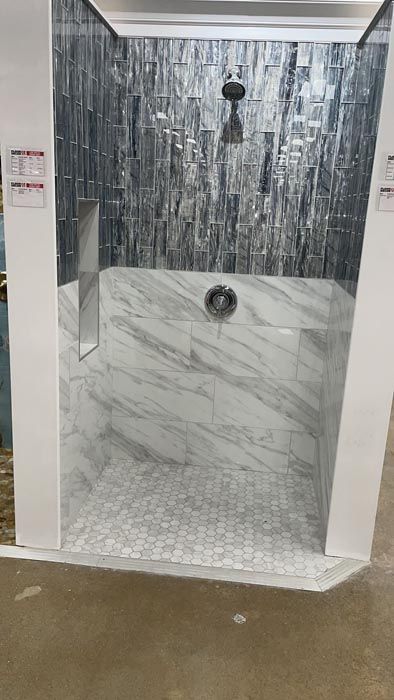 Shower display with gray marble-look walls, dark tile accent, and white tile floor in a store showroom