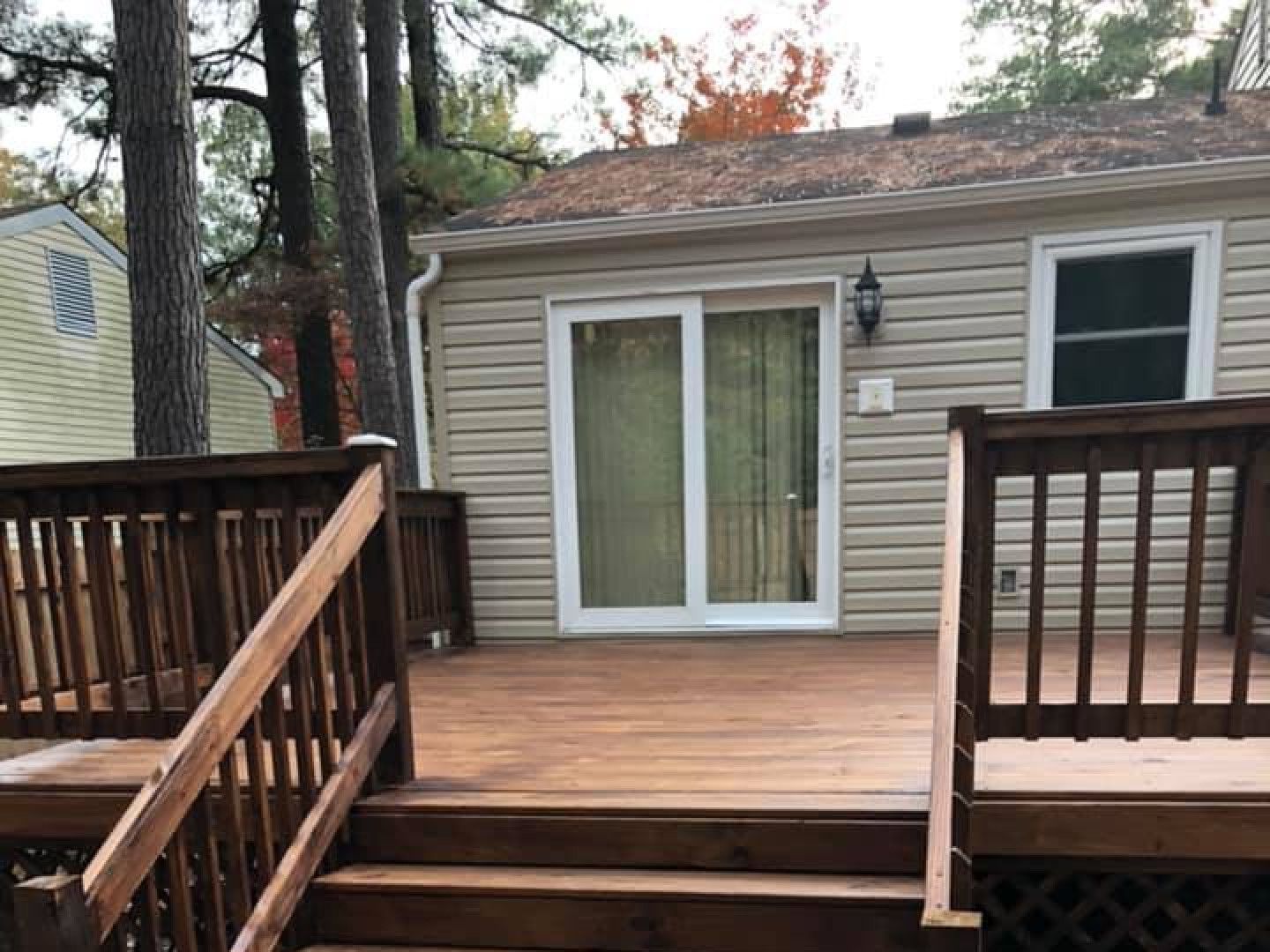 Wooden back deck with railing and sliding glass door on a beige house