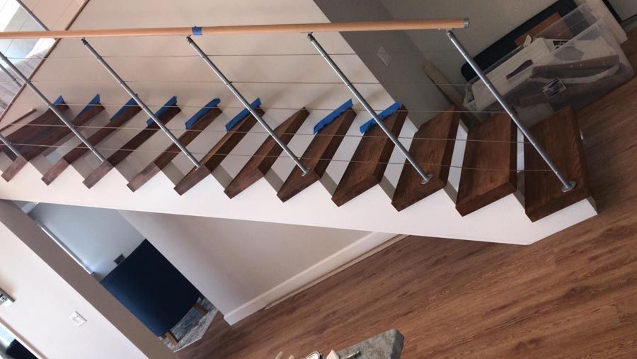Modern staircase with wooden steps, glass railing, and wood floor beneath.