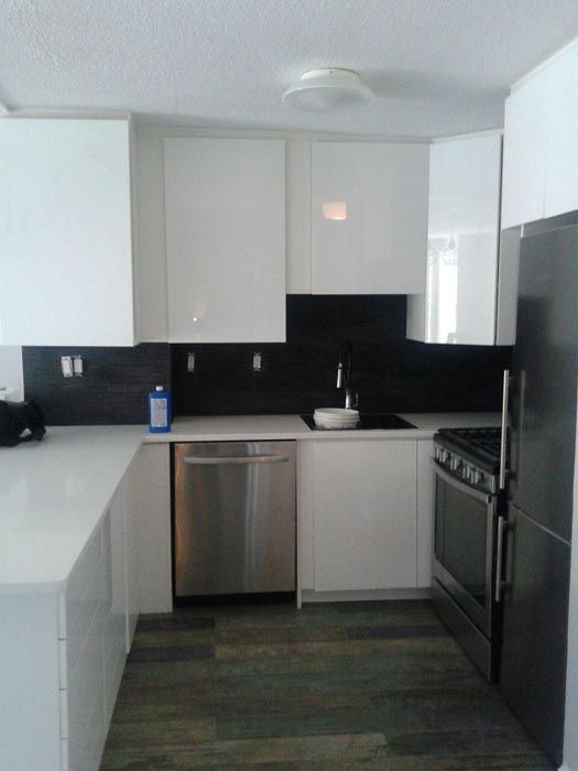 Modern kitchen with white cabinets, black backsplash, stainless dishwasher, and dark wood floor