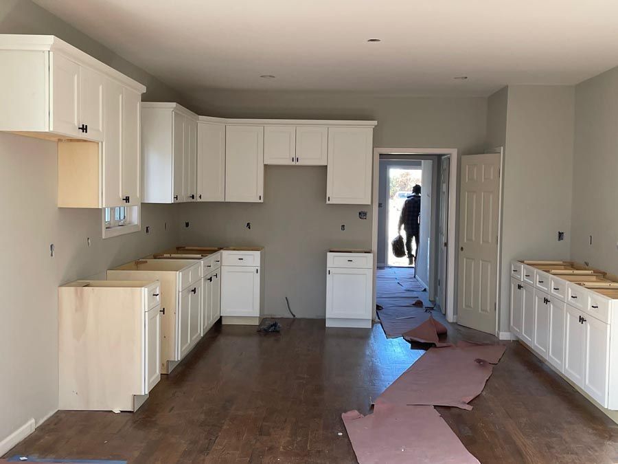 Empty kitchen with white cabinets, dark wood floor, and pink protective paper leading to a doorway.
