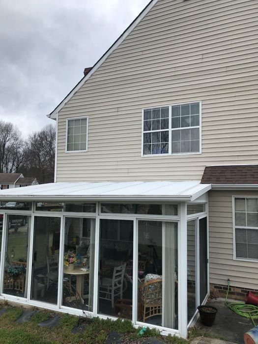 Back of beige house with white sunroom enclosure and snow on the roof