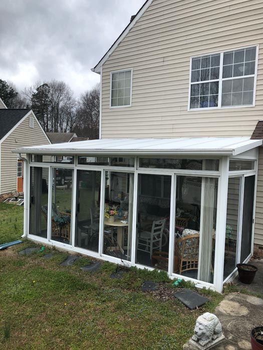 White sunroom addition with glass walls and slanted roof attached to a beige house.