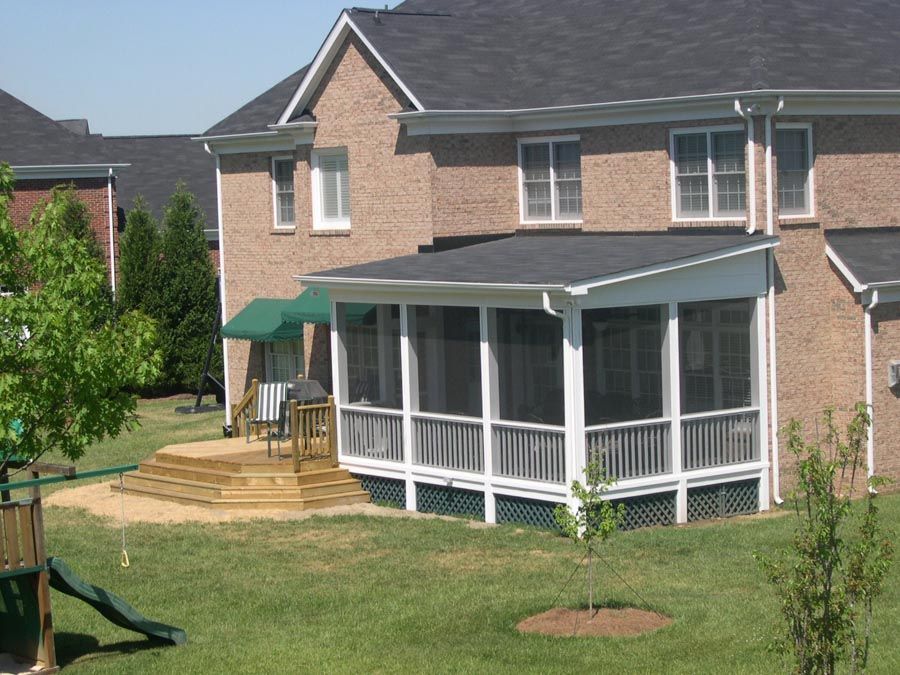 Backyard of a brick house with a screened porch, wooden deck, lawn, and trees