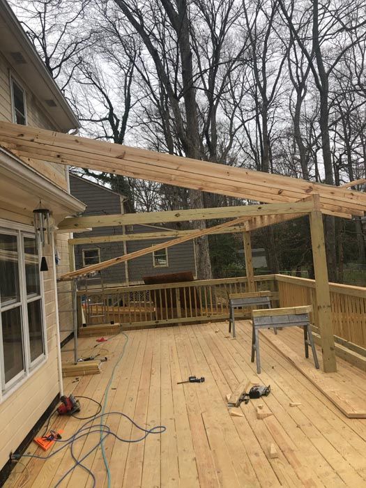 Back deck under construction with exposed rafters, unfinished floor, and tools scattered around.