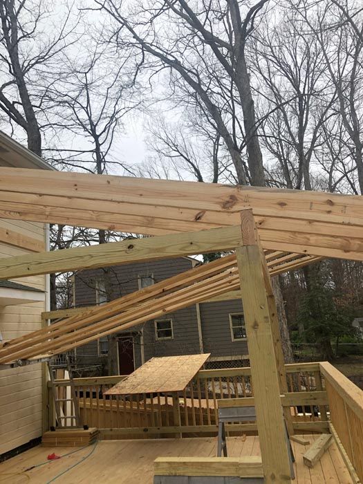 Partially built wooden deck frame with beams and posts in a backyard, bare trees overhead