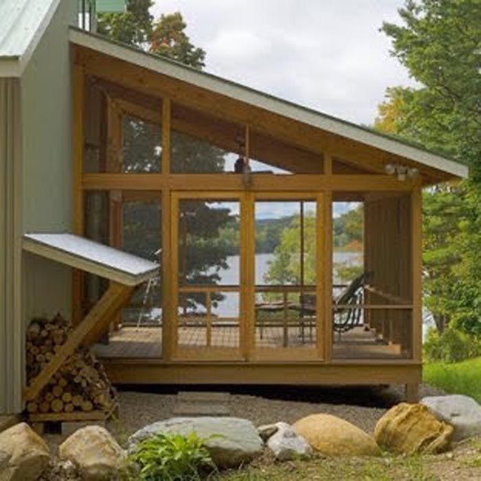 Modern lakeside cabin deck with large windows, sloped roof, and stacked firewood under the overhang