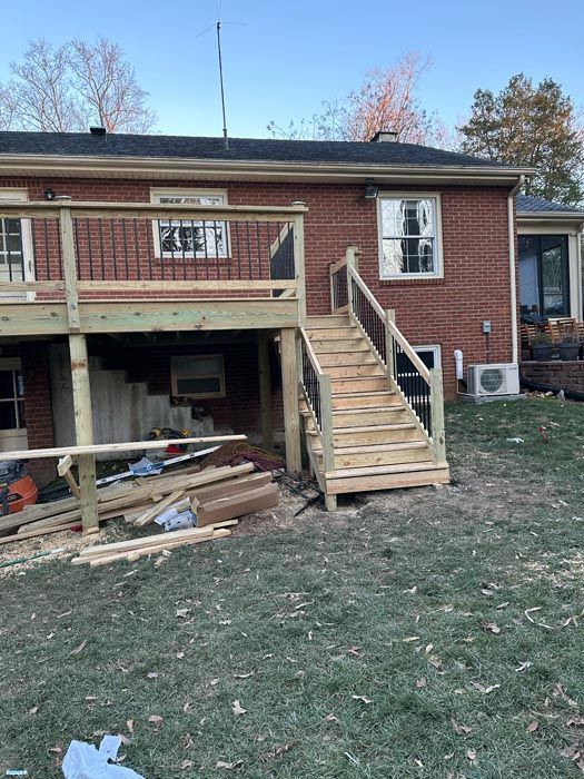 Backyard of a brick house with a raised deck, wooden stairs, and construction debris below
