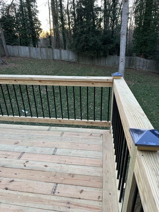 Wooden deck corner with black railings overlooking a grassy yard and trees at dusk
