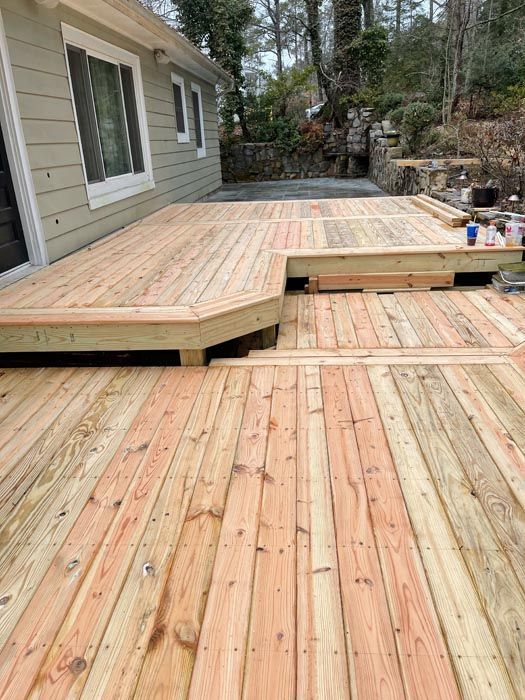 Wooden deck under construction beside a house, with steps and railing in a wooded backyard.