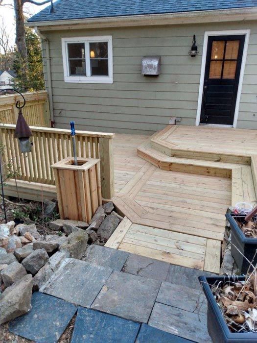 Wooden ramp and steps leading to a back door beside a gray house and rock garden