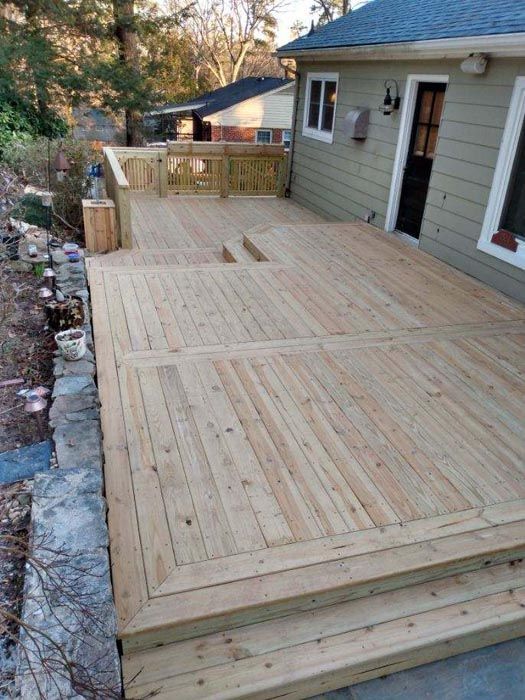 Wooden backyard deck with steps beside a house, bordered by stone and landscaping.