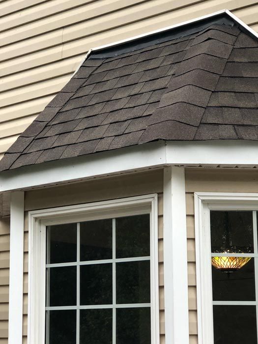 Exterior corner of a house with a shingled roof, white trim, and a windowed porch overhang
