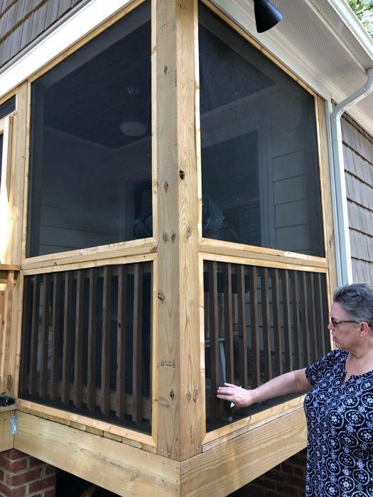 Screened wooden porch corner with a person touching the frame outdoors