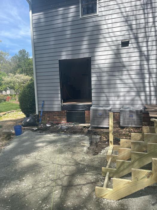 Side of gray house with open doorway, gravel yard, and wooden steps under construction.