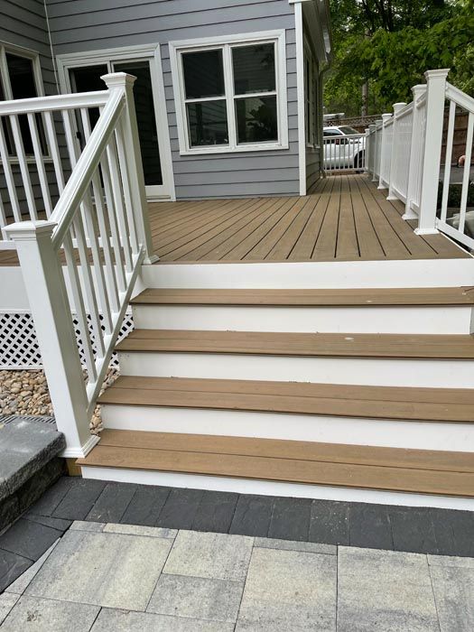 Front steps with white railings leading to a gray house deck and doorway