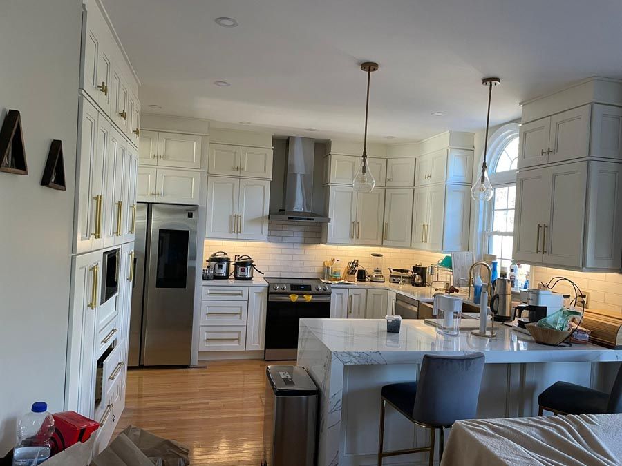 Bright white kitchen with island, stainless fridge, pendant lights, and a breakfast bar by an arched window