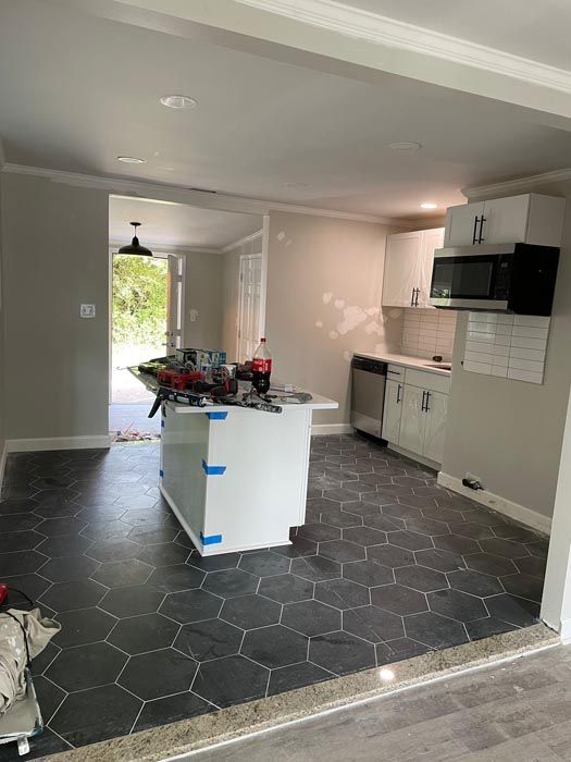 Kitchen interior with black hex tile floor, white cabinets, and a white island under renovation