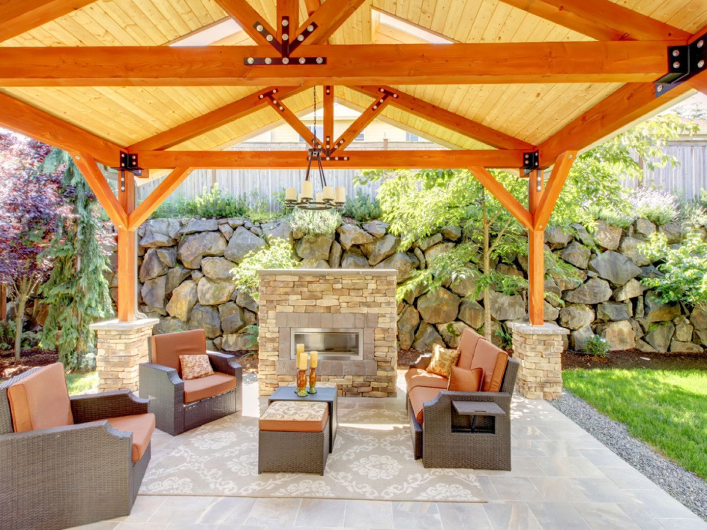 Covered patio with wooden beams, stone fireplace, and wicker seating around a coffee table