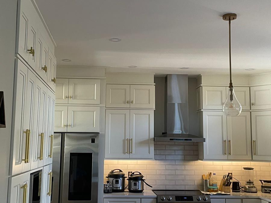 Bright white modern kitchen with cabinets, island, pendant light, and stainless steel hood stove.