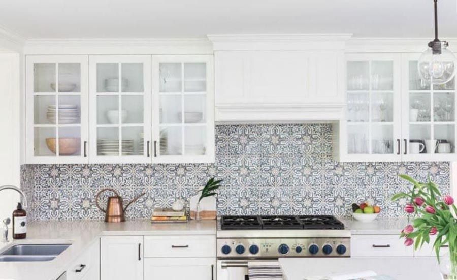 Bright white kitchen with patterned tile backsplash, open shelves, copper kettle, and a stainless stove.