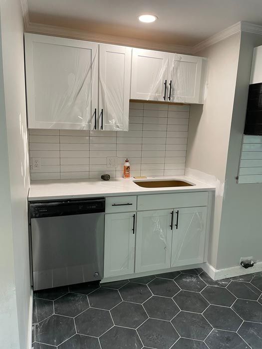 Small white kitchen with cabinets, sink, dishwasher, and hexagonal dark floor tiles