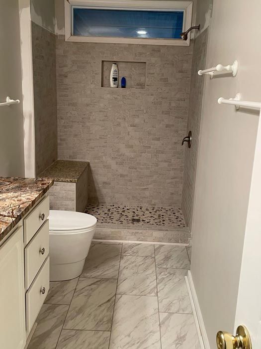 Small bathroom with toilet, granite vanity, tiled shower, and high window.