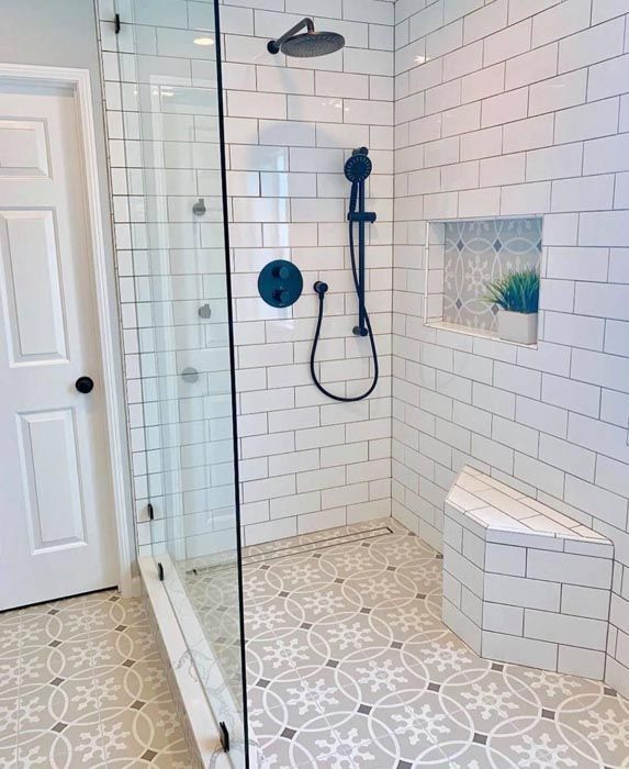 Walk-in shower with white subway tile, glass door, black fixtures, and patterned tile floor.