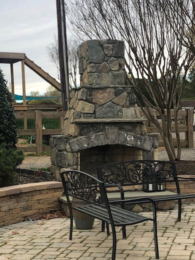 Stone outdoor fireplace with wrought-iron chairs on a patio, under overcast sky