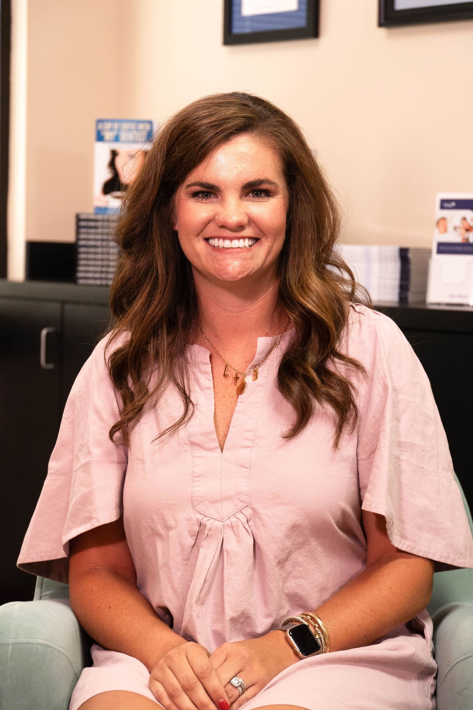 A woman in a pink dress is sitting in a chair and smiling.