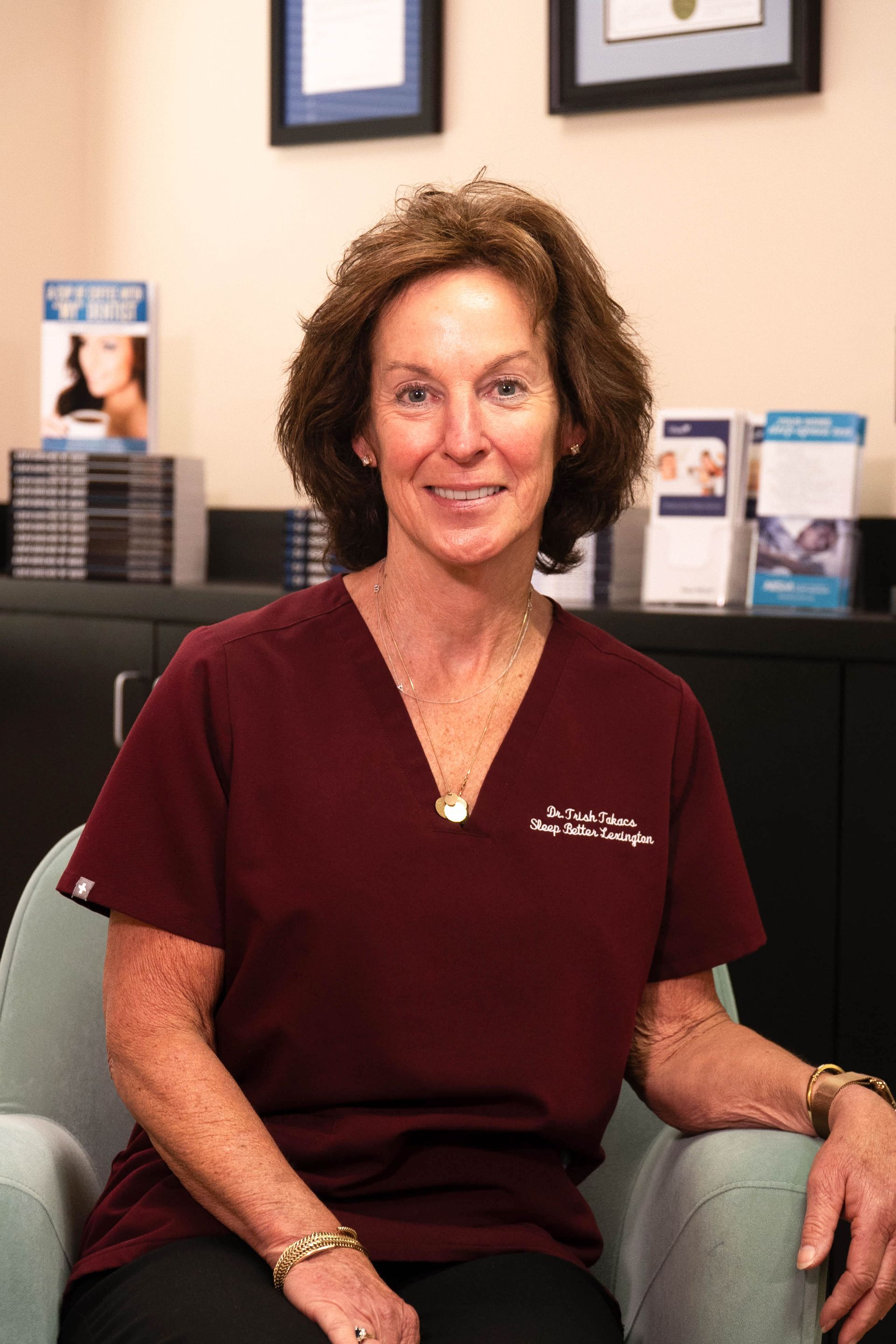 A woman in a maroon scrub top is sitting in a chair