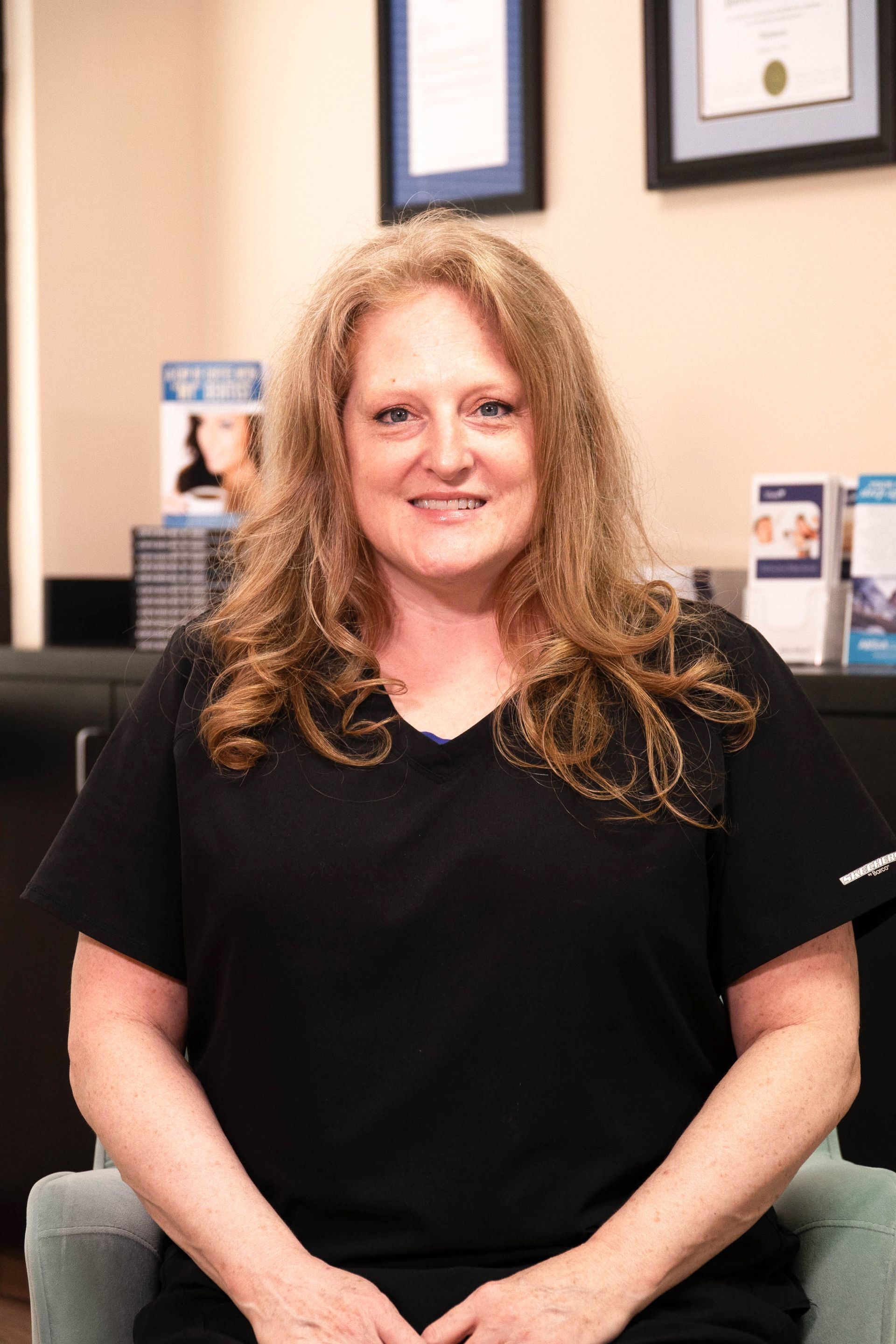 A woman in a black shirt is sitting in a chair and smiling.