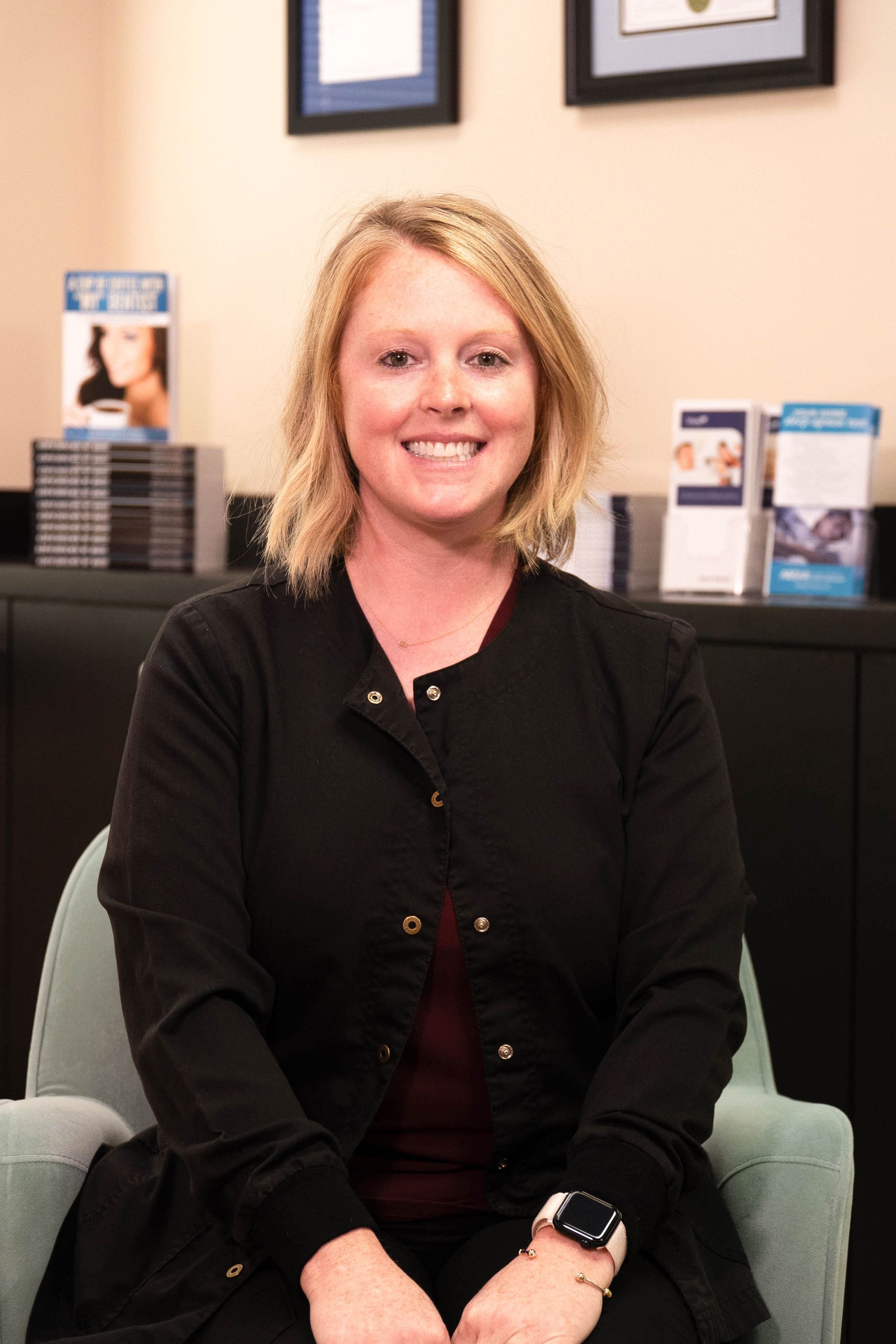 A woman is sitting in a chair and smiling for the camera.