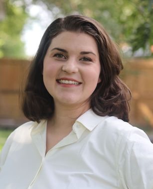 Smiling woman in a navy shirt standing against a plain light wall.