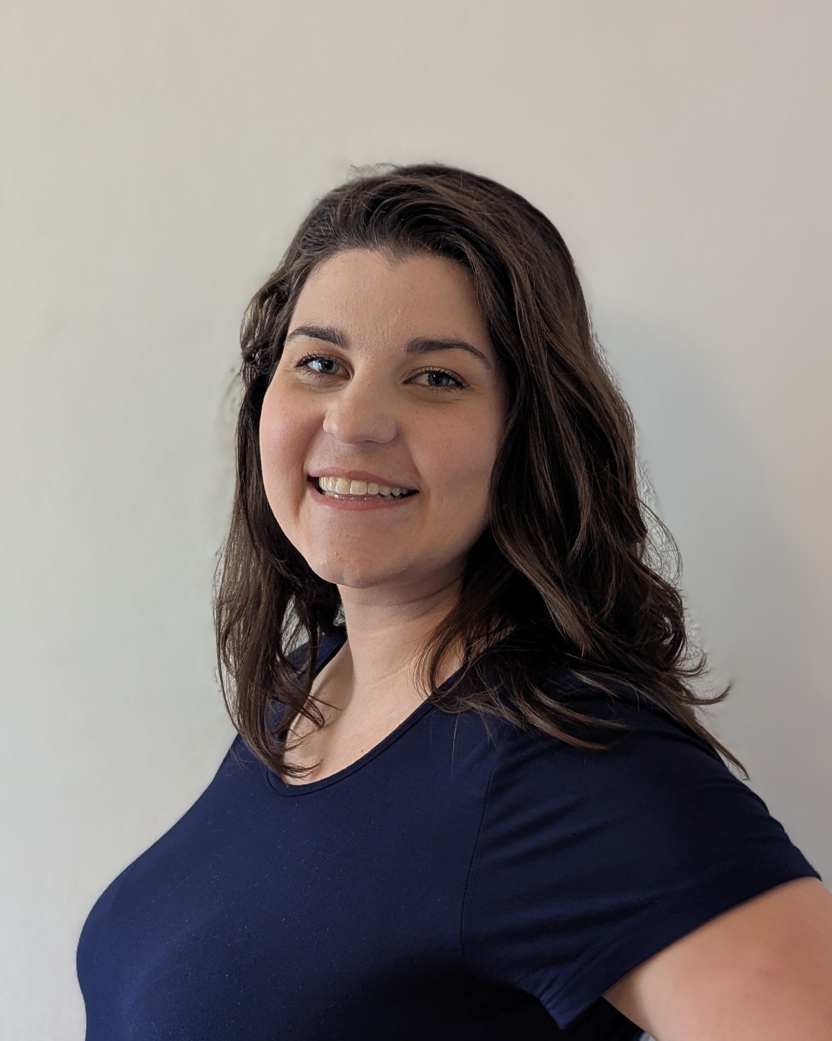 Smiling woman in a navy shirt standing against a plain light wall.