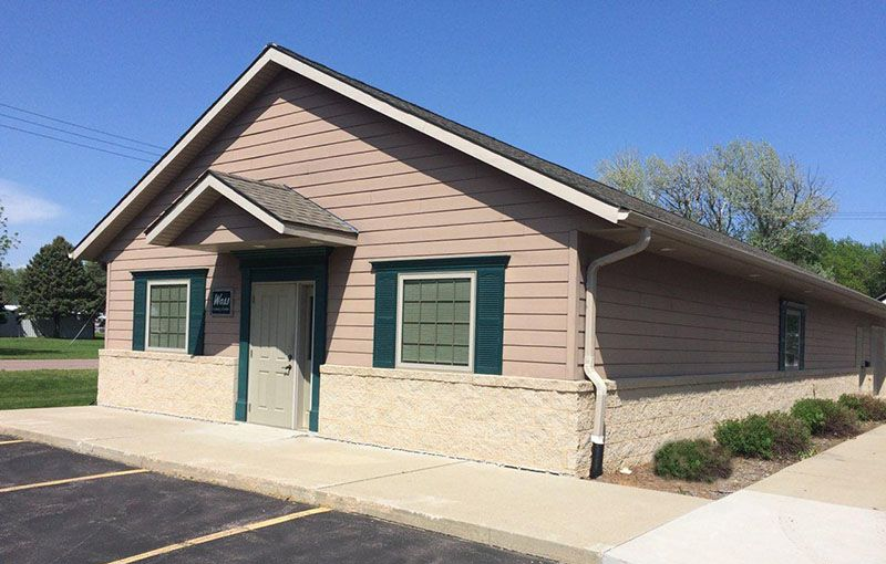 Tan and beige commercial building with green trim, sidewalk, and parking lot.
