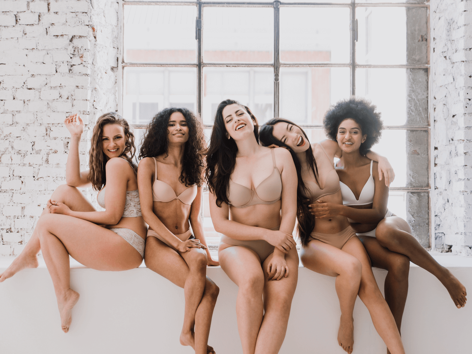 Un gruppo di donne in biancheria intima è seduto una accanto all'altra sul davanzale di una finestra.