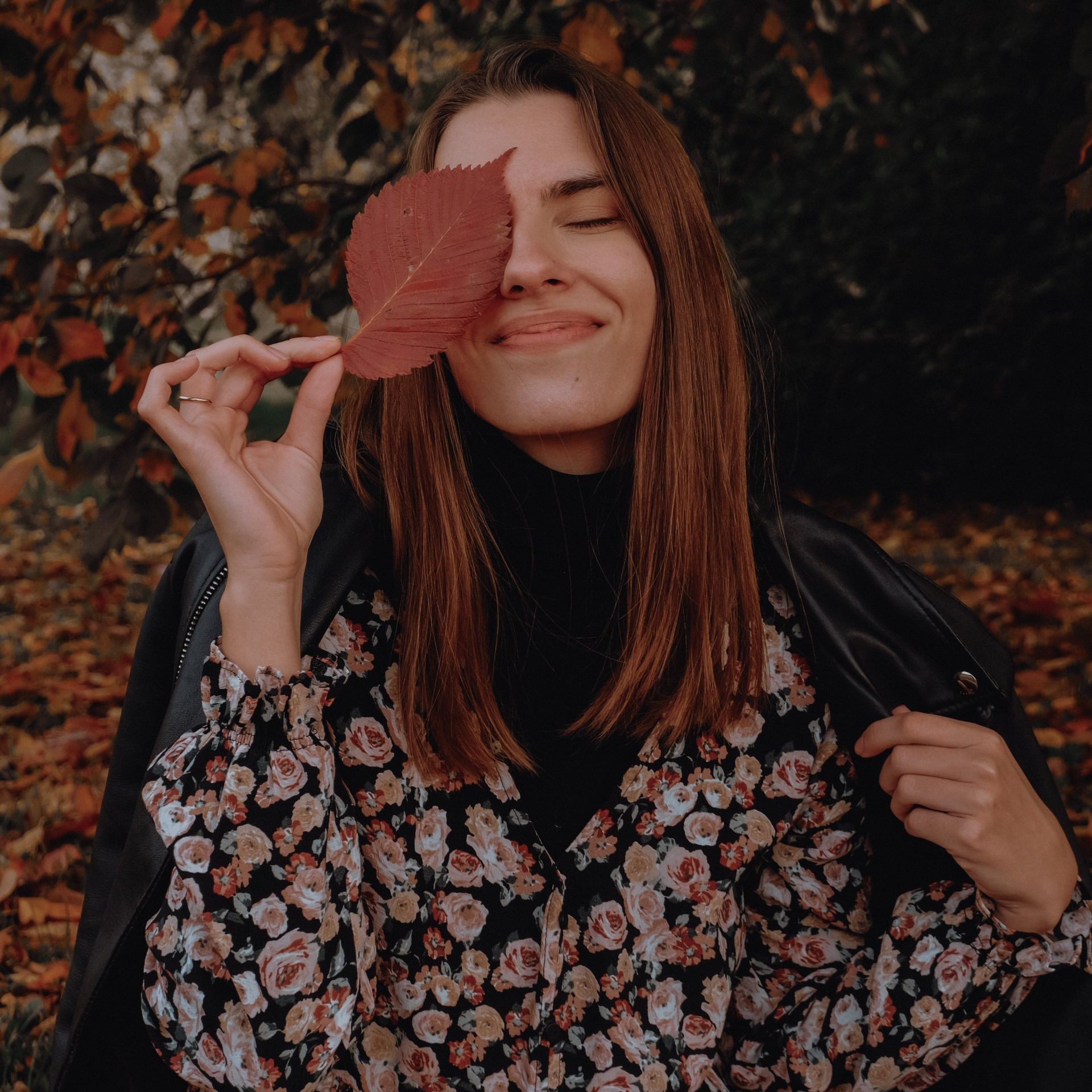 Una donna tiene una foglia rossa davanti al viso.