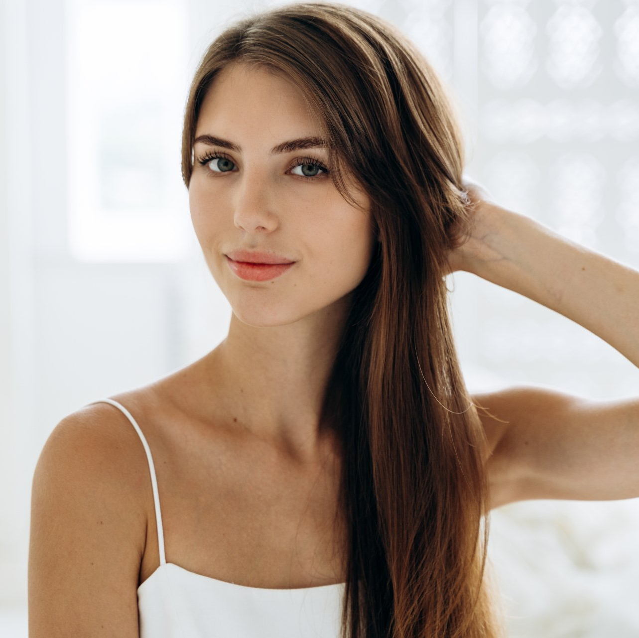Una donna con i capelli lunghi indossa una canottiera bianca.