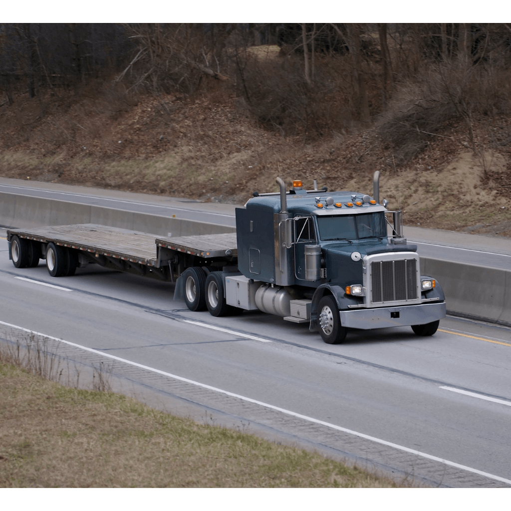 Blue semi truck hauling a flatbed trailer on a rural highway