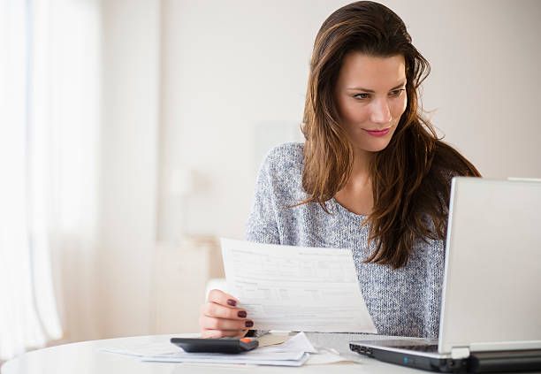 Woman reviewing papers beside a laptop at a bright table