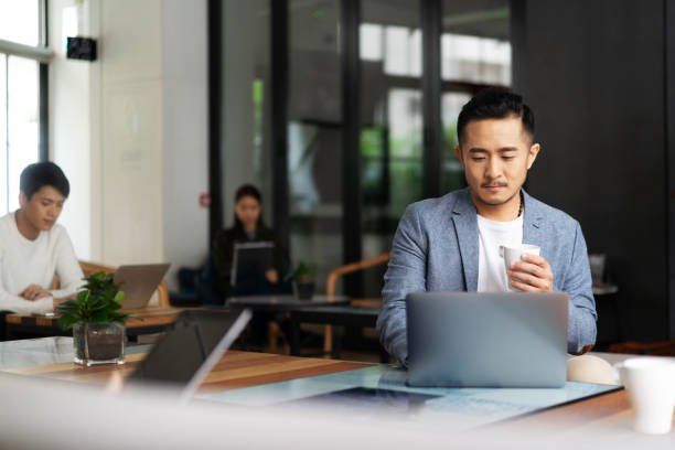 People working in a modern office, with a man using a laptop in the foreground.