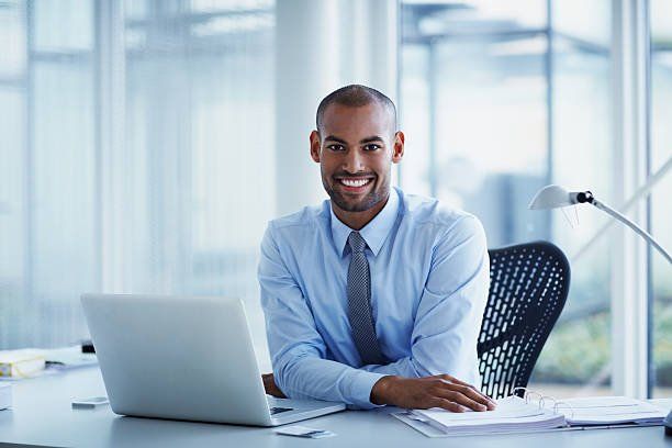 Smiling professional seated at a desk with a laptop in a bright office