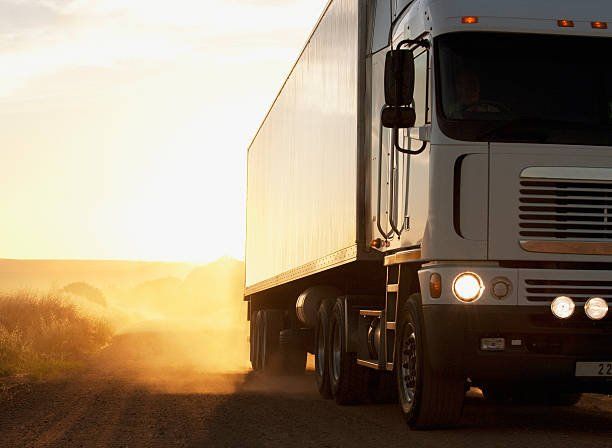 Semi-truck driving on a dusty road at sunset