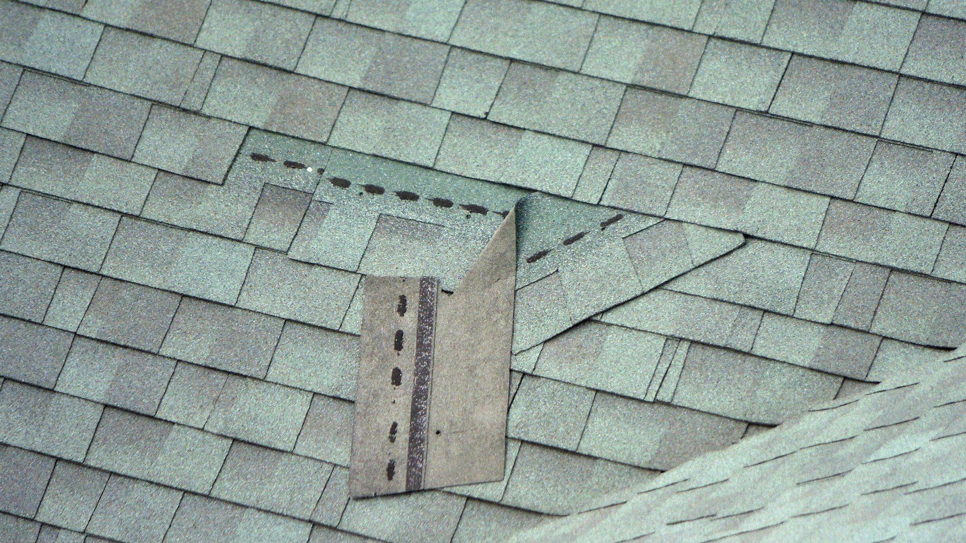 Close-up of asphalt shingles on a roof with a metal flashing repair.