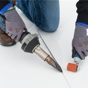 Person using a hot air tool to weld a white roof seam, rolling seam with a small roller.