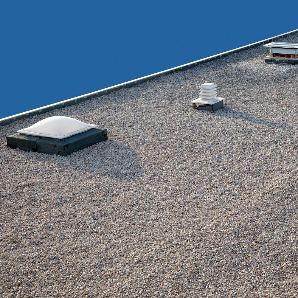 Gravel-covered flat roof with skylights and vents against a blue sky.