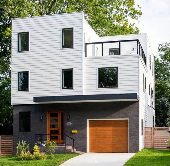 Modern three-story house with gray brick base, white siding, and wood garage door.