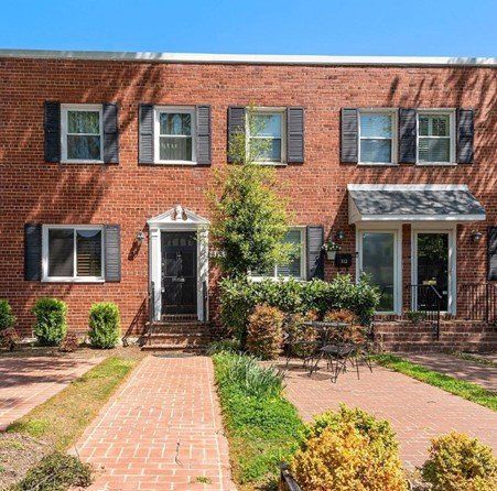 Red brick townhouses with black shutters and a small front yard, clear blue sky.