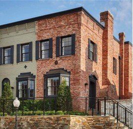 Multi-story brick building with black shutters and door, small fence, and outdoor staircase.